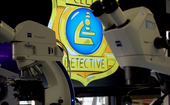 Two microscopes with the cell detectives emblem in the background
